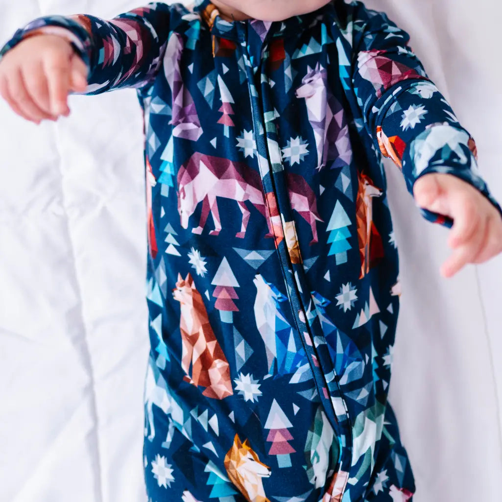 Close up of the front zipper and chest of a zip up baby pajama in a navy print of geometric wolves, triangle pine trees, and snowflakes.